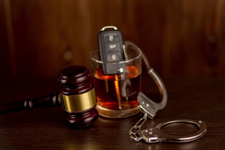 Keys sitting in a glass on whiskey next to gavel
