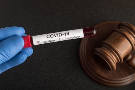 blue-gloved hand holding positive COVID-19 test above black desk with gavel on it