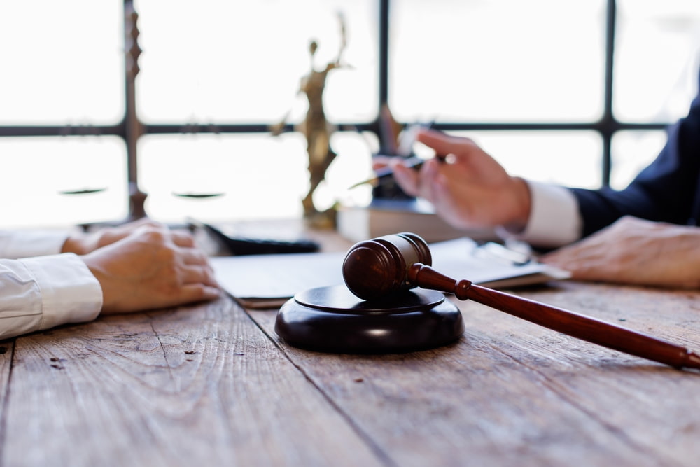 Attorney reviewing paperwork with a client at a desk beside a wooden gavel and a Lady Justice statue.