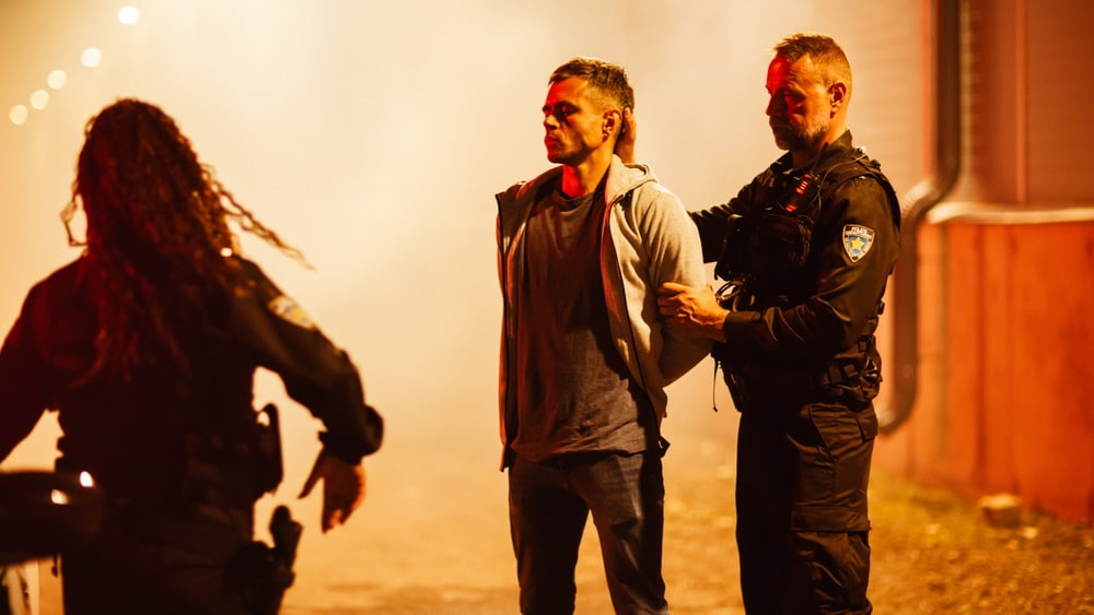 A man being detained by police officers at night.