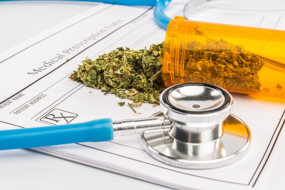 Cannabis buds spilling from a prescription bottle onto a medical prescription form beside a stethoscope.